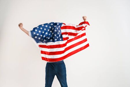Celebrating an Independence day. Stars and Stripes. Young man with the flag of the United States of America isolated on white studio background. Looks crazy happy and proud as a patriot of his country.の写真素材