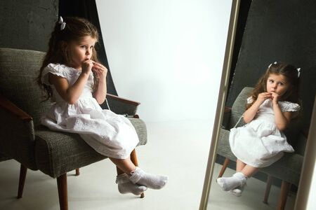 Interaction of children with adult world. Cute girl trying to do bright make up for being older. Little female model trying on mums cosmetics at home. Childhood, style, fashion, dream concept.の写真素材