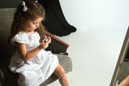 Interaction of children with adult world. Cute girl trying to do bright make up for being older. Little female model trying on mums cosmetics at home. Childhood, style, fashion, dream concept.の写真素材