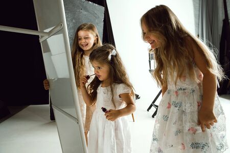 Interaction of children with adult world. Cute girls trying to do bright make up for being older....
