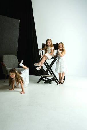 Interaction of children with adult world. Cute girls wearing mums oversize shoes and dress for being older like she is. Little female models trying on clothes at home. Childhood, style, dream concept.の写真素材