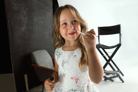 Interaction of children with adult world. Cute girl trying to do bright make up for being older. Little female model trying on mums cosmetics at home. Childhood, style, fashion, dream concept.の写真素材