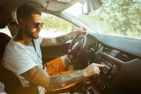 Young man preparing for vacation trip on the car in sunny day. Male model sitting and ready for...