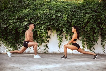 A muscular athletes doing workout at the park. Gymnastics, training, fitness workout flexibility. Summer city in sunny day on background field. Active and healthy lifestyle, youth, bodybuilding.の写真素材