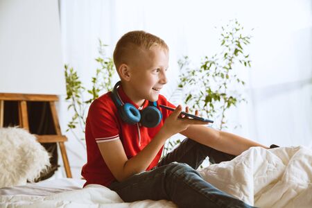 Boy using different gadgets at home. Little model with smart watches, smartphone or tablet and headphones. Making selfie, chating, gaming, watching videos. Interaction of kids and modern technologies.の写真素材