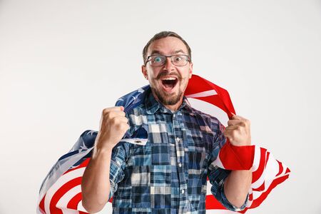 Celebrating an Independence day. Stars and Stripes. Young man with the flag of the United States of America isolated on white studio background. Looks crazy happy and proud as a patriot of his country.の写真素材