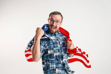 Celebrating an Independence day. Stars and Stripes. Young man with the flag of the United States of America isolated on white studio background. Looks crazy happy and proud as a patriot of his country.の写真素材