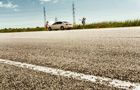 The young couple broke down the car while traveling on the way to rest. They are trying to stop...