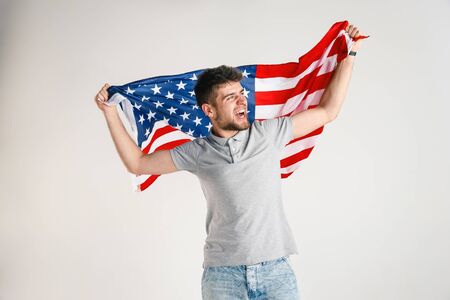 Celebrating an Independence day. Stars and Stripes. Young man with the flag of the United States of America isolated on white studio background. Looks crazy happy and proud as a patriot of his country.の写真素材