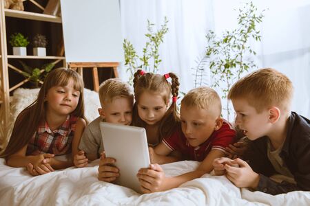 Boys and girls using different gadgets at home. Childs with smart watches, smartphone and...