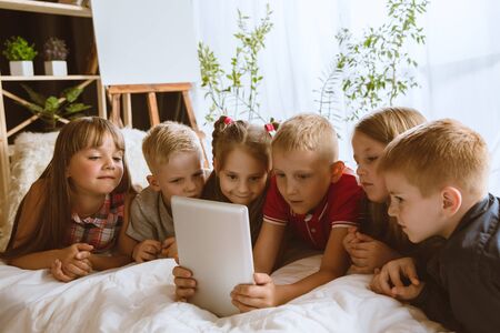 Boys and girls using different gadgets at home. Childs with smart watches, smartphone and...