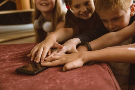 Boys and girls using different gadgets at home. Childs with smart watches, smartphone and...