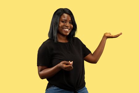 Young african-american woman isolated on yellow studio background, facial expression. Beautiful female half-length portrait. Concept of human emotions, facial expression. Choosing and inviting.の写真素材