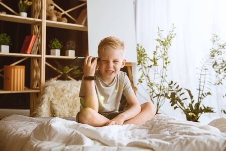 Boy using different gadgets at home. Little model with smart watches, smartphone or tablet and headphones. Making selfie, chating, gaming, watching videos. Interaction of kids and modern technologies.の写真素材