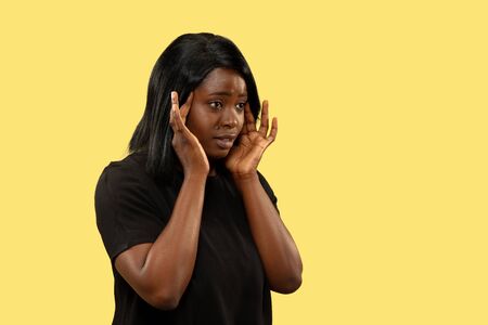 Young african-american woman isolated on yellow studio background, facial expression. Beautiful female half-length portrait. Concept of human emotions, facial expression. Suffering from headache.の写真素材