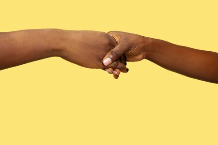 Close up shot of human holding hands isolated on yellow studio background. Concept of human relations, friendship, partnership, family. Copyspace.の写真素材