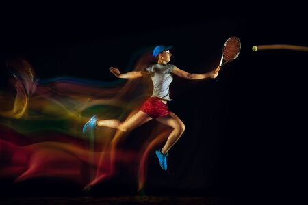One caucasian woman playing tennis isolated on black background in mixed and stobe light. Fit young...