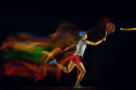 One caucasian woman playing tennis isolated on black background in mixed and stobe light. Fit young female player in motion or action during sport game. Concept of movement, sport, healthy lifestyle.の写真素材