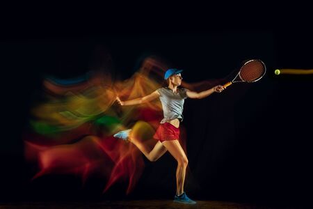 One caucasian woman playing tennis isolated on black background in mixed and stobe light. Fit young female player in motion or action during sport game. Concept of movement, sport, healthy lifestyle.の写真素材