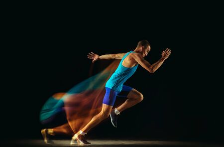 Professional male runner training isolated on black studio background in mixed light. Man in sportsuit practicing in run or jogging. Healthy lifestyle, sport, workout, motion and action concept.の写真素材