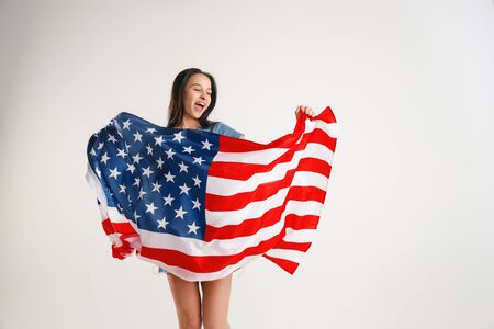 Celebrating an Independence day. Stars and Stripes. Young woman with the flag of the United States of America isolated on white studio background. Looks crazy happy and proud as a patriot of her country.の写真素材