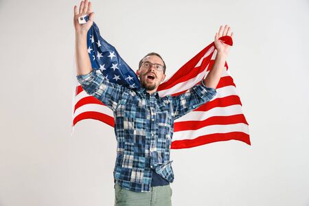 Celebrating an Independence day. Stars and Stripes. Young man with the flag of the United States of America isolated on white studio background. Looks crazy happy and proud as a patriot of his country.の写真素材