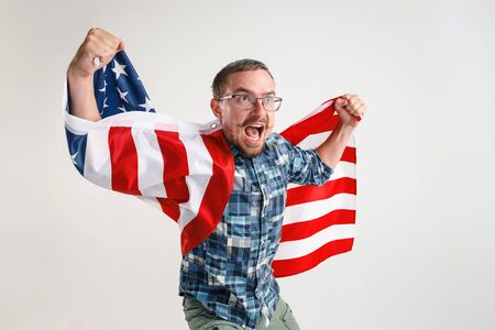 Celebrating an Independence day. Stars and Stripes. Young man with the flag of the United States of America isolated on white studio background. Looks crazy happy and proud as a patriot of his country.の写真素材