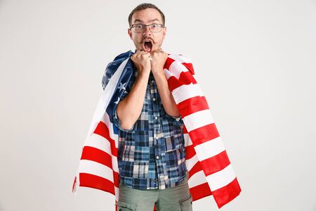 Celebrating an Independence day. Stars and Stripes. Young man with the flag of the United States of America isolated on white studio background. Looks crazy happy and proud as a patriot of his country.の写真素材