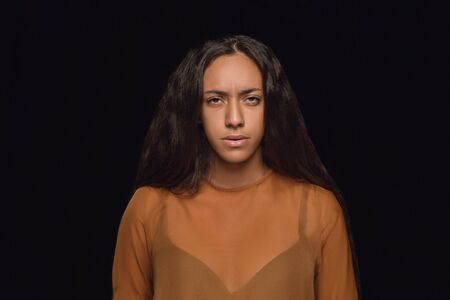 Close up portrait of young african-american woman isolated on black studio background. Photoshot of real emotions of female model. Facial expression, human nature. Sadness, look serious.の写真素材