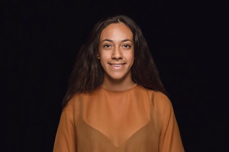 Close up portrait of young african-american woman isolated on black studio background. Photoshot of real emotions of female model. Facial expression, human nature. Standing and smiling.の写真素材