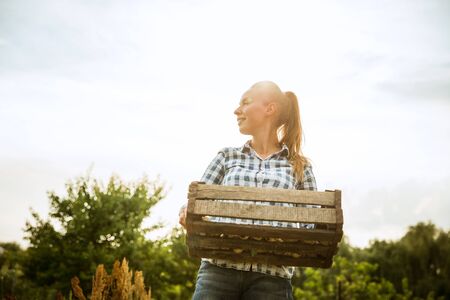 Young farmer working at her garden in sunny day. Woman engaged in the cultivation of eco friendly products. Concept of farming, agriculture, healthy lifestyle, harvesting of natural nutrition.の写真素材