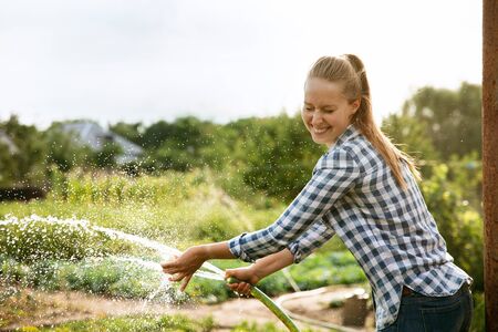 Young farmer working at her garden in sunny day. Woman engaged in the cultivation of eco friendly products. Concept of farming, agriculture, healthy lifestyle, growing natural nutrition by its own.の写真素材