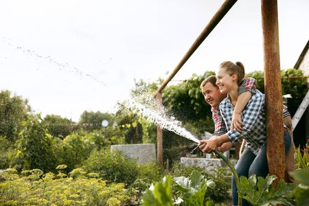 Young and happy farmers couple at their garden in sunny day. Man and woman engaged in the cultivation of eco friendly products. Concept of farming, agriculture, healthy lifestyle, family occupation.の写真素材