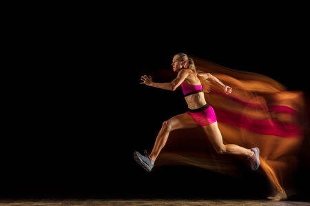Professional female relay racer training isolated on black studio background in mixed light. Woman...