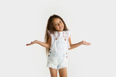 Beautiful female half-length portrait isolated on white studio background. Little emotional asian girl wearing white. Facial expression, human emotions, advertising concept. Showing, inviting.の写真素材