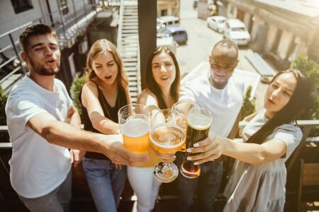 Young group of friends drinking beer, having fun, laughting and celebrating together. Women and men with beers glasses in sunny day. Oktoberfest, friendship, togetherness, happiness, summer concept.の写真素材
