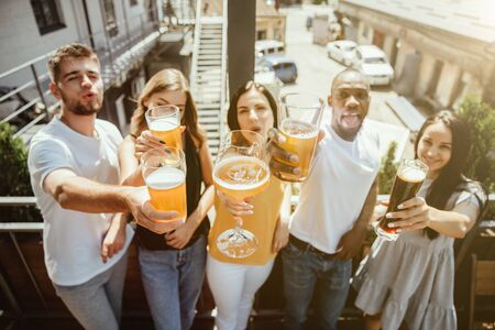 Young group of friends drinking beer, having fun, laughting and celebrating together. Women and men with beers glasses in sunny day. Oktoberfest, friendship, togetherness, happiness, summer concept.の写真素材