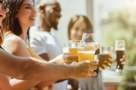 Young group of friends drinking beer, having fun, laughting and celebrating together. Women and men with beers glasses in sunny day. Oktoberfest, friendship, togetherness, happiness, summer concept.の写真素材