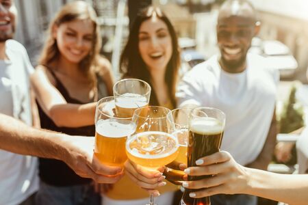 Young group of friends drinking beer, having fun, laughting and celebrating together. Women and men with beers glasses in sunny day. Oktoberfest, friendship, togetherness, happiness, summer concept.の写真素材