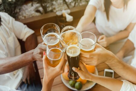 Young group of friends drinking beer, having fun, laughting and celebrating together. Women and men with beers glasses in sunny day. Oktoberfest, friendship, togetherness, happiness, summer concept.の写真素材