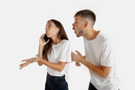 Beautiful young couples portrait isolated on white studio background. Facial expression, human emotions, advertising concept. Woman talking on the phone, man wants to pay her attention on hisself.の写真素材