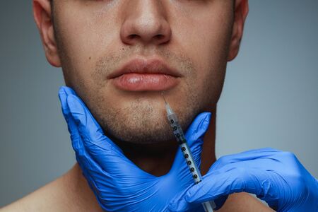 Close-up portrait of young man isolated on grey studio background. Filling botox surgery procedure. Concept of mens health and beauty, cosmetology, self-care, body and skin care. Anti-aging.の写真素材
