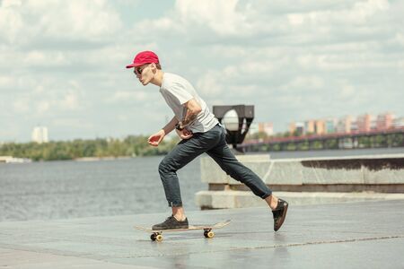 Skateboarder doing a trick at the citys street in sunny day. Young man in sneakers and cap riding...
