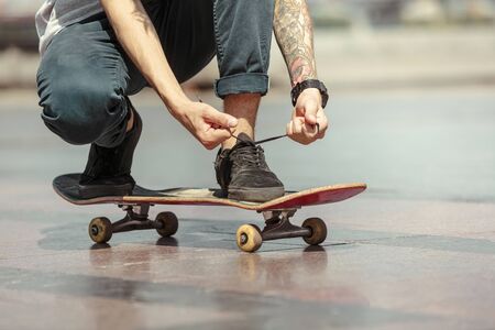 Skateboarder preparing for riding at the citys street in sunny day. Young man in sneakers and cap...