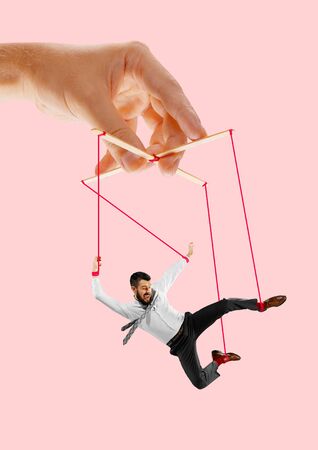 Man like a puppet in somebodies hands on coral background. Concept of unfair manipulation, phycology of exploitation, mental technique, motivation. Puppets and their masters. Possessive relationship.の写真素材