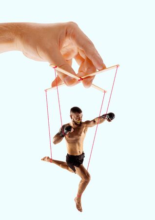 Man like a puppet in somebodies hands on blue background. Concept of unfair manipulation, phycology of exploitation, mental technique, motivation. Puppets and their masters. Possessive relationship.の写真素材