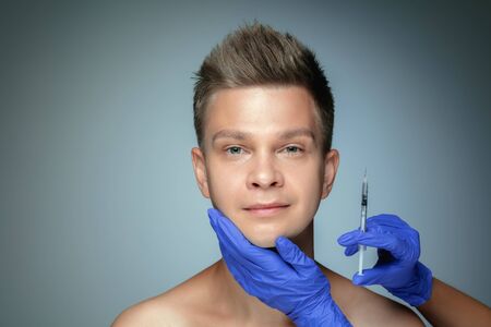 Close-up portrait of young man isolated on grey studio background. Filling surgery procedure, lips...