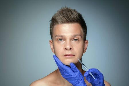Close-up portrait of young man isolated on grey studio background. Filling surgery procedure, lips and cheekbones. Concept of mens health and beauty, cosmetology, body and skin care. Anti-aging.の写真素材