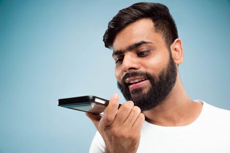 Half-length close up portrait of young hindoo man in white shirt on blue background. Human emotions,...