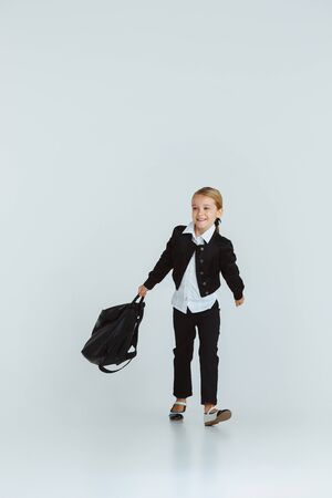 Girl preparing for school after a long summer break. Back to school. Little female caucasian model posing in schools uniform with backpack on white background. Childhood, education, holidays concept.の写真素材